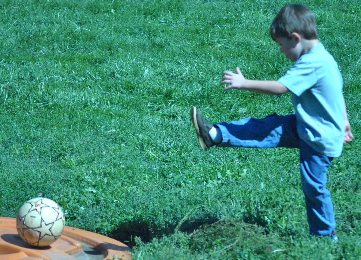 The preschoolers spend their time outside on this sunny day kicking the soccer ball around. 