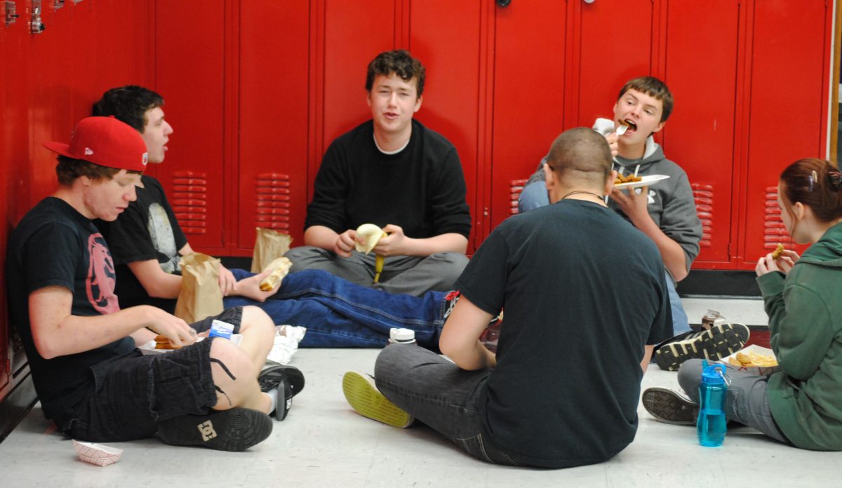 A group of students eat their lunches against the lockers near the school store. Photo by Dean Trail.