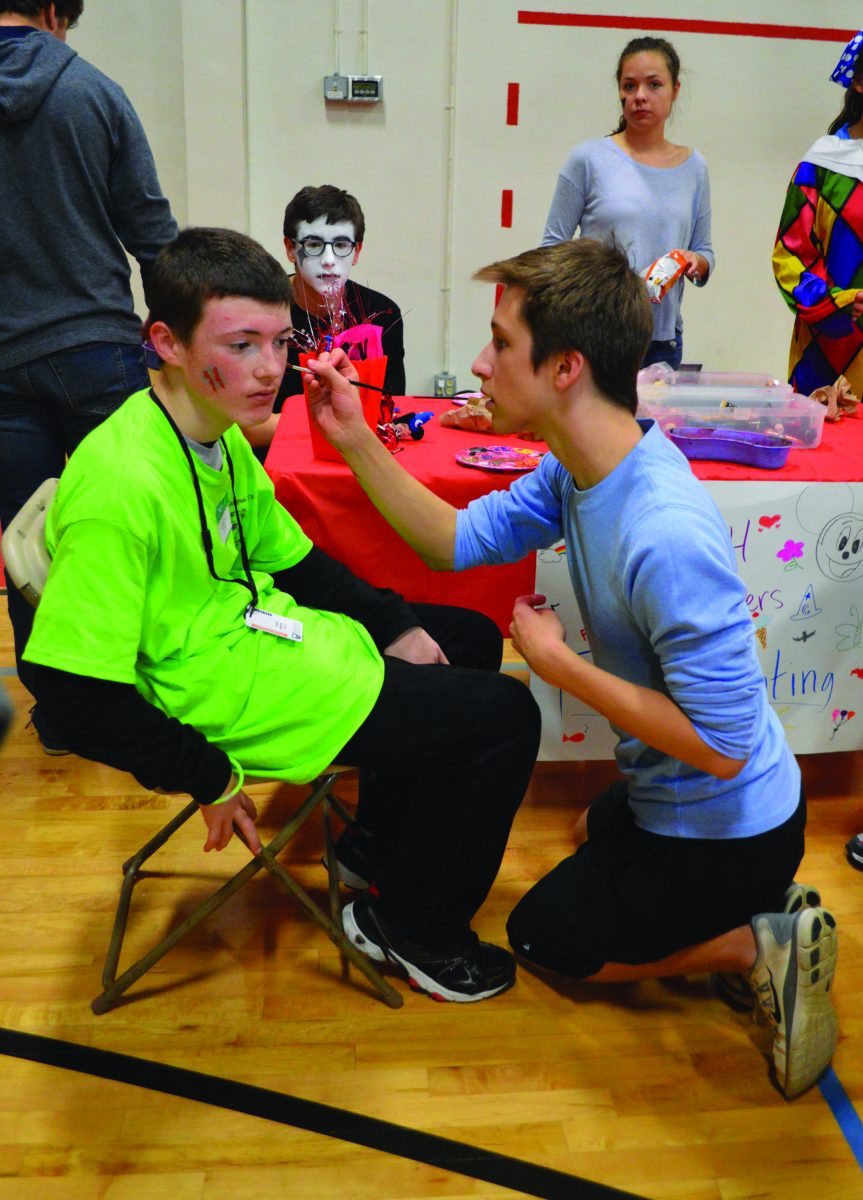 Sophomore Evan Mogley paints a design on an athlete’s face at the carnival in Gym B on Oct. 22. The Drama Club provided a face painting booth.  Photo by Ilennah Fanega.