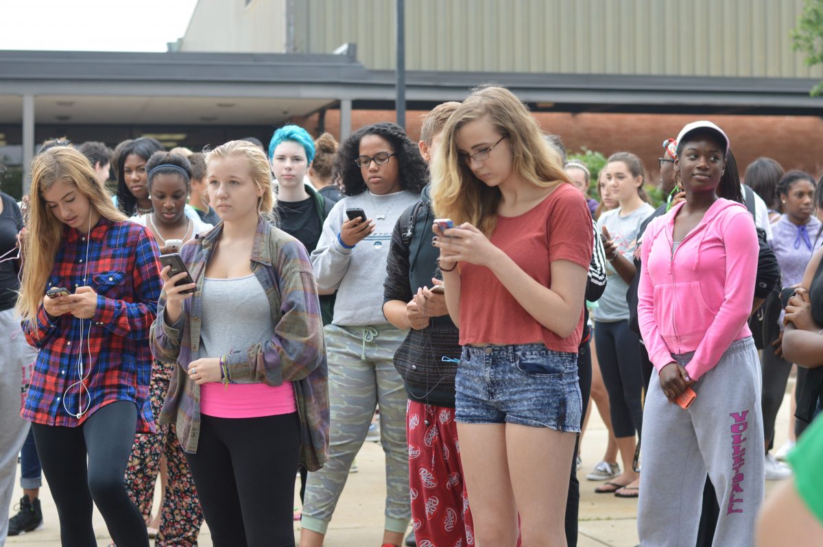 A group of protesters stand on their phones during the first walkout held on Sept. 10, outside of school by the flag pole. Students posted words of support on Twitter and Vines of the walkout on social media. Photo by Piper Rother.