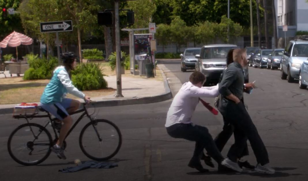 Deluca pulling Jackson and Maggie away from a speeding car, while a teenager on a bike passes and is about to be hit.