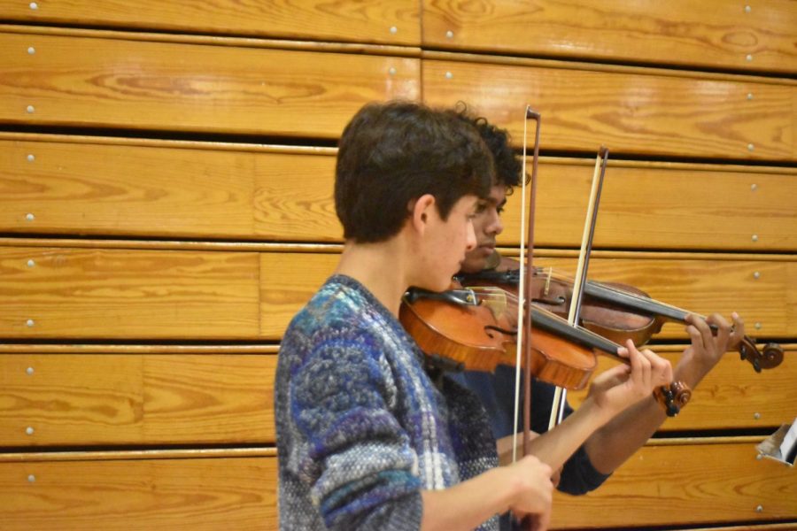Junior AJ Eisenberg and junior Akshaj Variath play violin at the orchestra table. The orchestra is planning their trip to Carnegie Hall in April. 